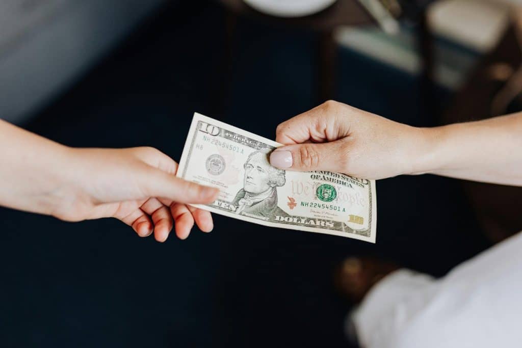 How Long Does Debt Collection Stay on Your Credit Report? Timelines Explained 4 Two hands exchanging a ten-dollar bill against a dark background.