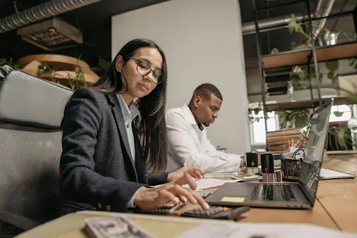 How to Deal with Debt Collection Agencies: Best Practices & Handling Disputes 3 Two professionals working at a desk with a laptop and a calculator in a modern office space