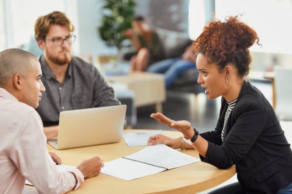 How to Deal with Debt Collection Agencies: Best Practices & Handling Disputes 4 Woman gestures while discussing documents with two men across a table in a modern office setting