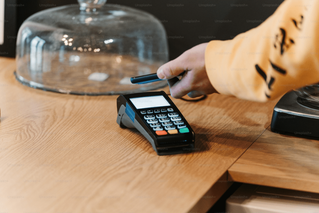 Can a Chargeback Be Sent to Collections? 3 Hand holding a payment card near a card reader terminal.