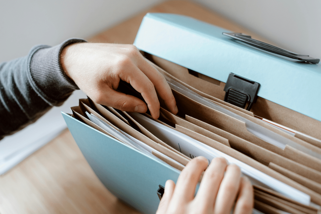 B2B Debt Collection in Sugar Land, TX: Best Companies, Cost & Reviews 6 Hands reaching into a light blue desktop file organizer containing multiple manila folders.