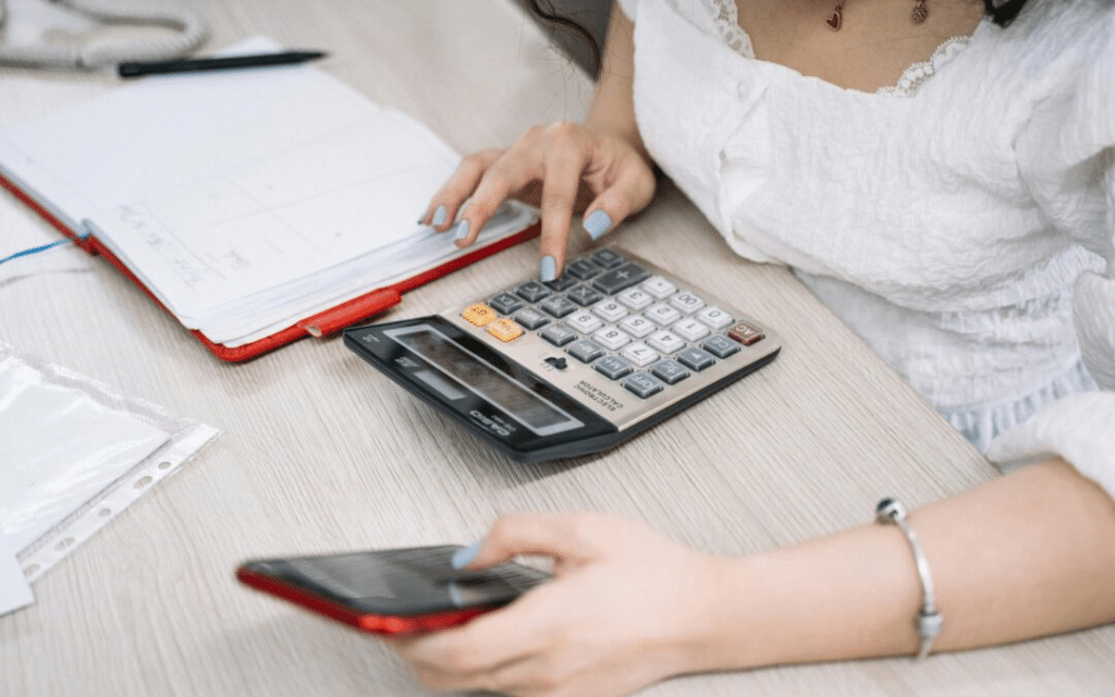Accounts Receivable Aging Report: Examples, Templates & Guide (2026) 4 Woman using a calculator while holding a smartphone at a desk with documents.