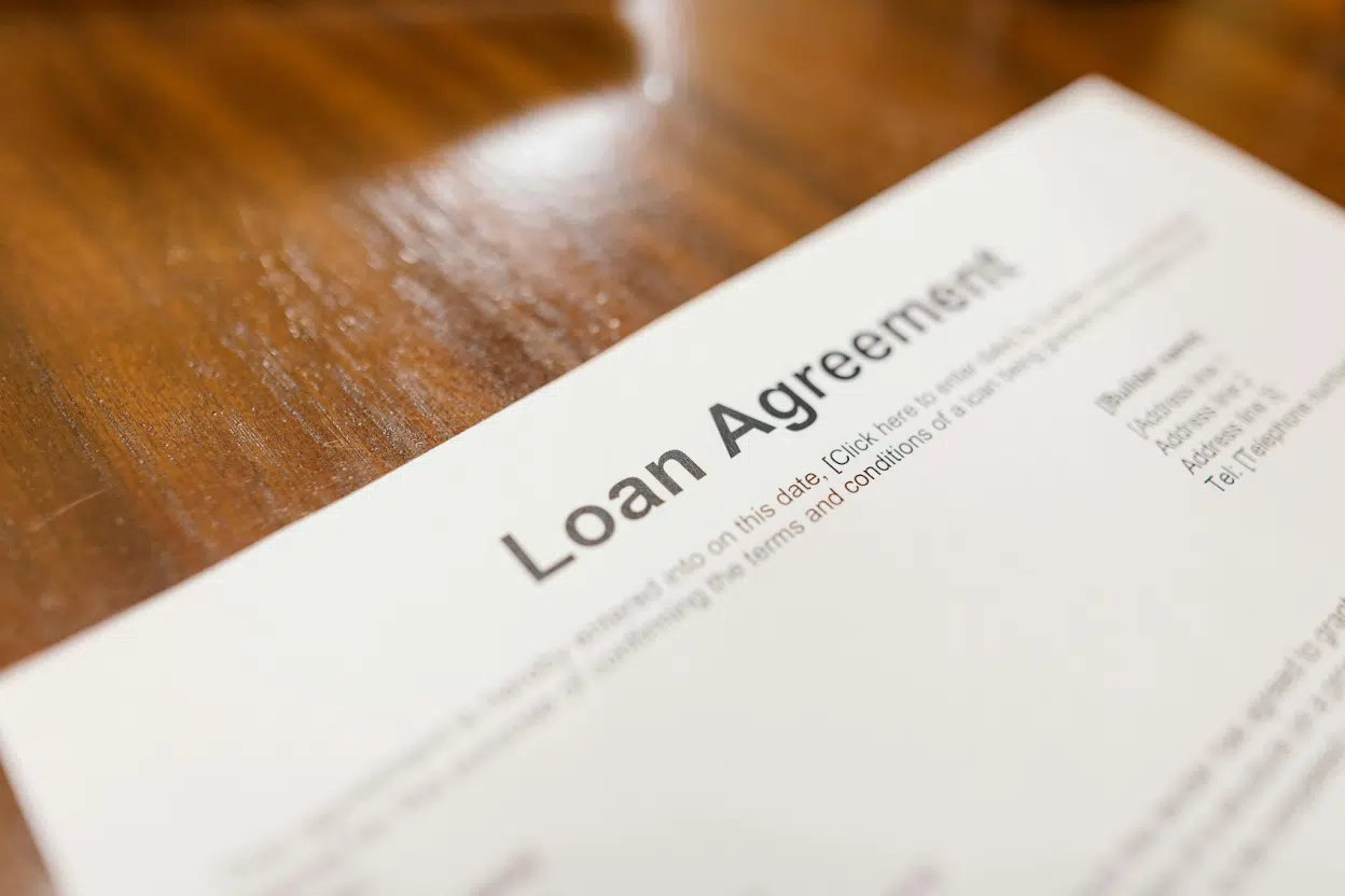 Auto Lender Collection Services 1 A loan agreement document resting on a polished wooden table, with visible text fields