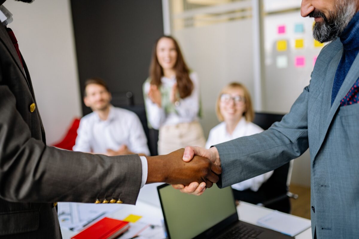 Accounts Receivable Risk Management: Examples & Solutions 4 Two businessmen shake hands in an office as colleagues smile and applaud in the background.